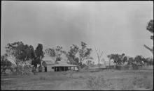 A black and white photograph of a few small buildings at Beagle Bay. In between the buildings there are many trees.