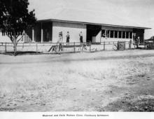 A black and white photograph of a building at Cherbourg Dormitory. There is a small group of people standing in front of the building.