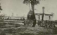 A black and white photograph of a building at Cootamundra Girls' Home. Standing in front of the building there are a group of residents and staff members.
