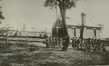 A black and white photograph of a building at Cootamundra Girls' Home. Standing in front of the building there are a group of  residents and  staff members.