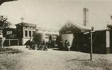 A black and white photograph of the exterior of Coota Mundra Girls' Home. A group of residents and staff members are standing beside water holding tanks.