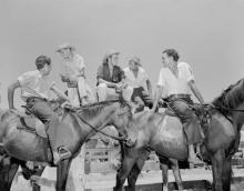 A black and white photograph of a group of young men at Croker Island Mission. Three are sitting on a fence, while two are on horseback.