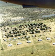 A colour photograph of Doomadgee Mission taken from an aeroplane. Buildings of various sizes, mostly small, are constructed in rows and spaced in regular intervals.