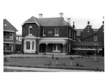A black and white photograph of the front face of a building at St Joseph's Sebastopol. The building is constructed from stone masonry and consists of two floors. The ground floor has a porch with ornate filigree latticework.
