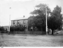 A black and white photograph of the front of Kennion House. The building has a brick face, and several trees which shield the ground floor windows from the street.