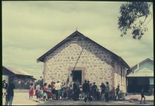 A colour photograph of a crowd at Marribank Mission. They are standing outside of a building with a stone-masonry façade.