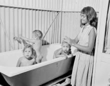 A black and white photograph of a small group of children at Retta Dixon Home. Three younger children are in a bath, while an older child is assisting them.