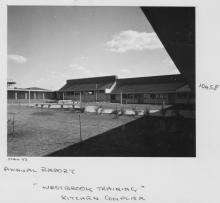 A black and white photograph of Westbrook Training Centre. On the photograph is written: May seventythree, Annual Report, Westbrook Training, Kitchen Complex. The kitchen building opens out into a large grassy space with several saplings.