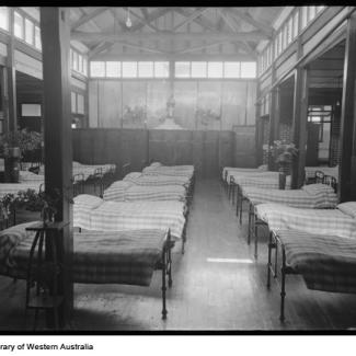 A black and white photograph of the dormitory at Castledare. A large number of metal framed beds occupy the room, and lying on top of each bed is an identical striped quilt. A statue of Mary and Jesus overlooks the beds.