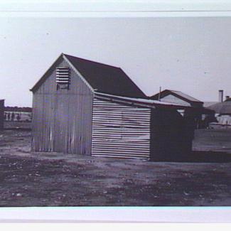 A black and white photograph of a small building at Colebrook Home. The building is constructed out of corrugated iron sheet metal, with a small vent near the roof. 