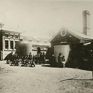 A black and white photograph of the exterior of Coota Mundra Girls' Home. A group of residents and staff members are standing beside water holding tanks.