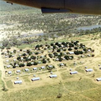 A colour photograph of Doomadgee Mission taken from an aeroplane. Buildings of various sizes, mostly small, are constructed in rows and spaced in regular intervals.
