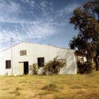 A colour photograph of a building at doomadgee Mission. The exterior of the building is constructed from corrugated iron sheet metal, with shutter windows.
