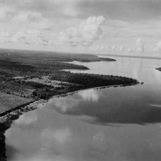 A black and white photograph of Garden Point Mission taken from an aeroplane. The shoreline of the Timor Sea is visible, along with Kings Cove as well as Harris Island.