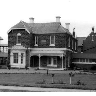 A black and white photograph of the front face of a building at St Joseph's Sebastopol. The building is constructed from stone masonry and consists of two floors. The ground floor has a porch with ornate filigree latticework.