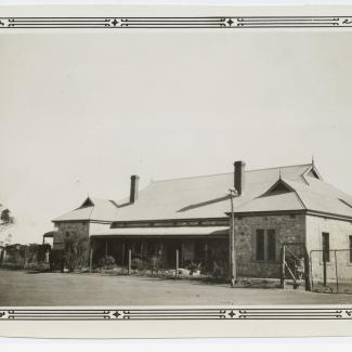 A black and white photograph of a building at Koonibba Lutheran Children's Home. The building has a stone-masonry face with a wire fence at the front.