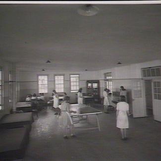 A black and white photograph of a room inside a building of Parramatta Girls' Industrial School. Inside the room are several girls, some of whom are playing table tennis, while others are at a piano.