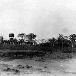 A black and white photograph of Roper River Mission. Several buildings are clustered together, with a water holding tank rising above the Mission.